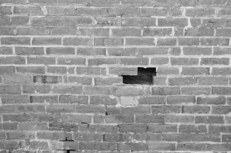 black and white image of a brick wall with a lone square hole