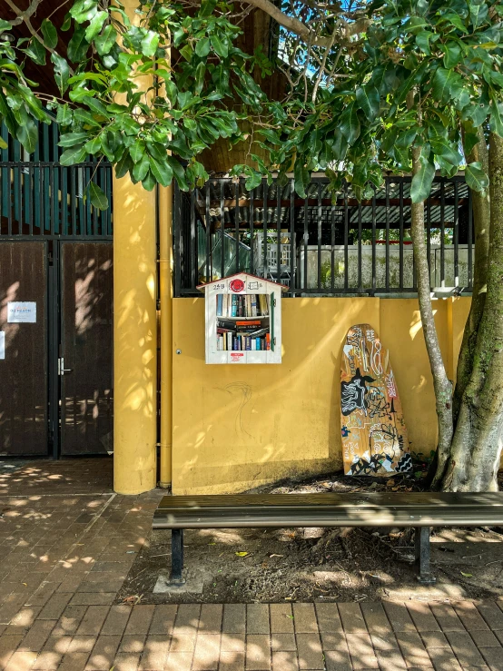 a bench sits against a yellow wall near a tree