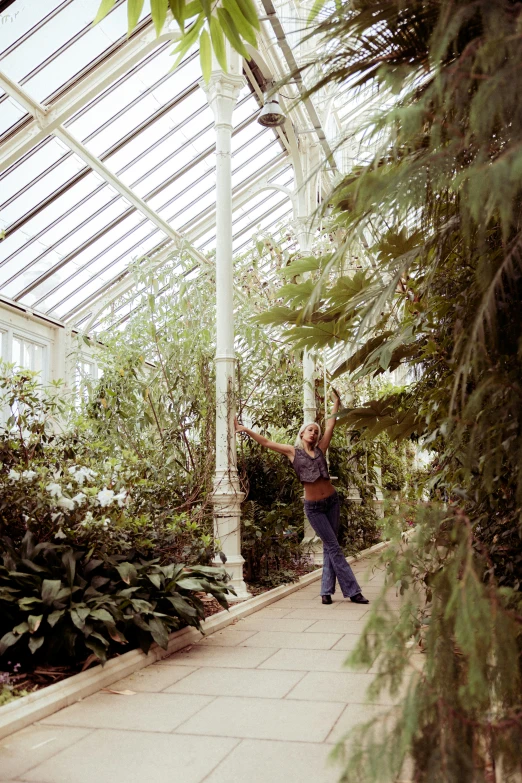 a woman holding her hands out as she stands in the greenhouse