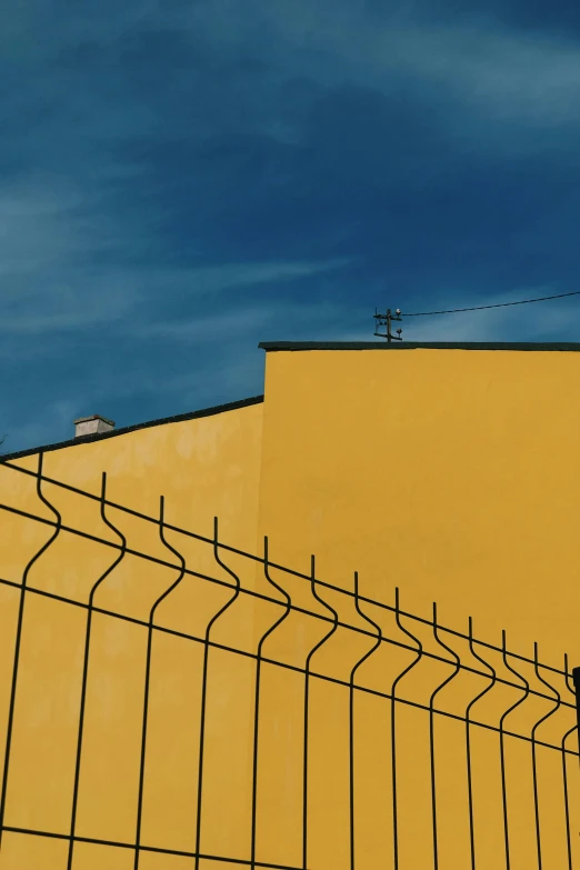 a bird standing on top of a fence next to a yellow building