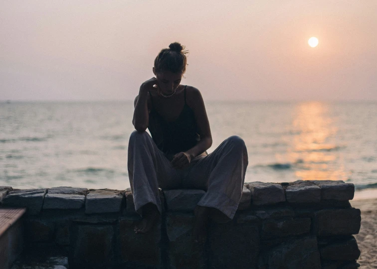 a woman sitting on a stone wall near the water