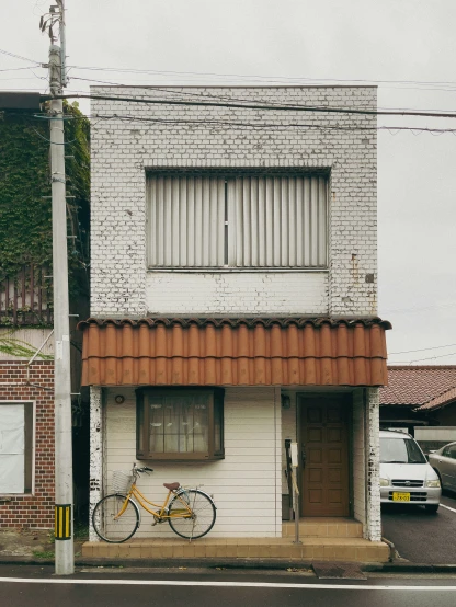 a white building with brown roof and a yellow bike parked outside