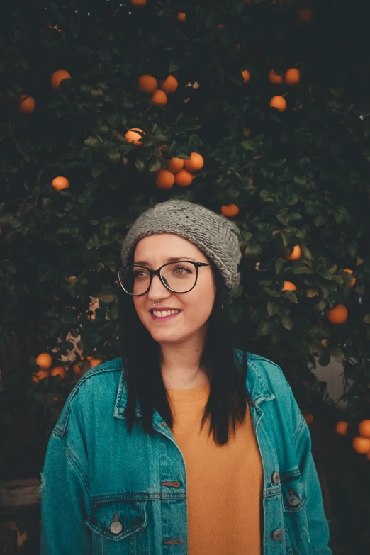 a woman in glasses and hat standing near orange trees