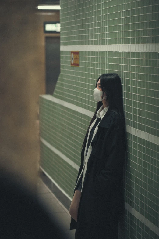 a woman wearing a face mask while standing next to a wall