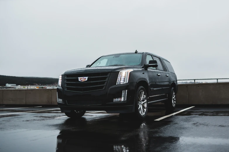 a black cadillac suv parked on a wet parking lot