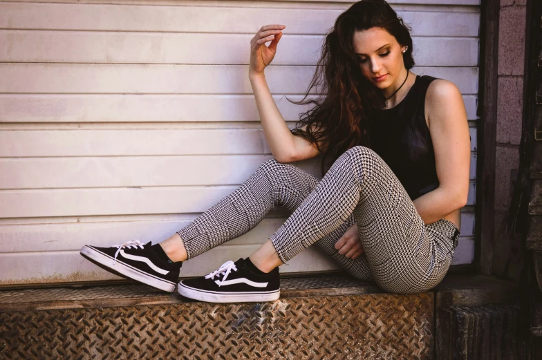 a woman sitting on the edge of a door and wearing black sneakers