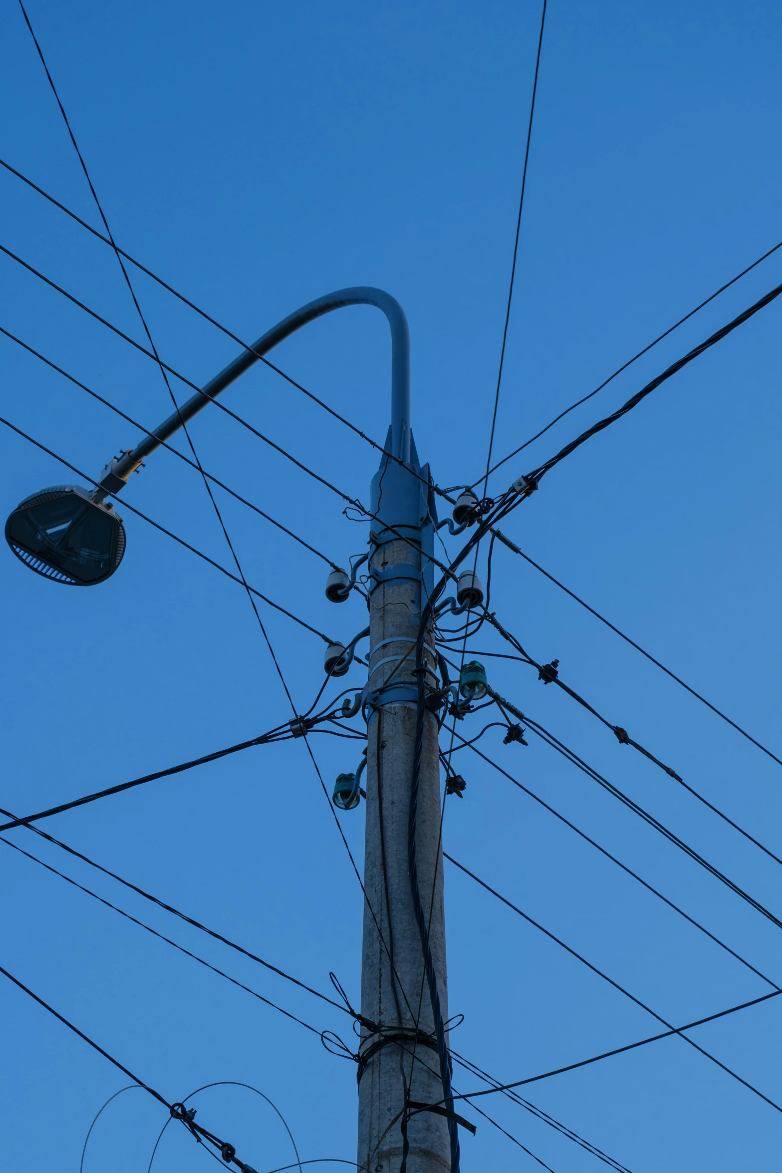 an electric pole and street lamp in silhouette against the blue sky