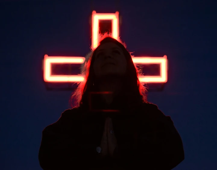 a woman standing in front of a cross lit up by red light