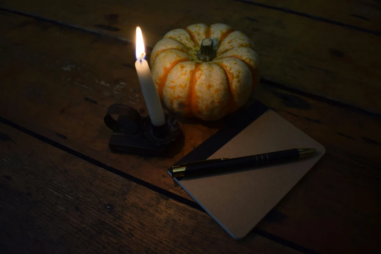 a lit candle is next to a notepad and a pumpkin