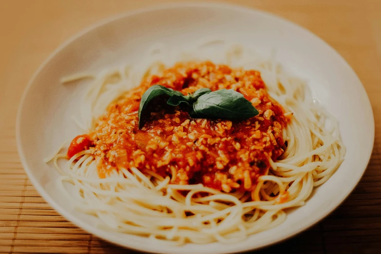 a white plate of pasta with a spinach leaf on top