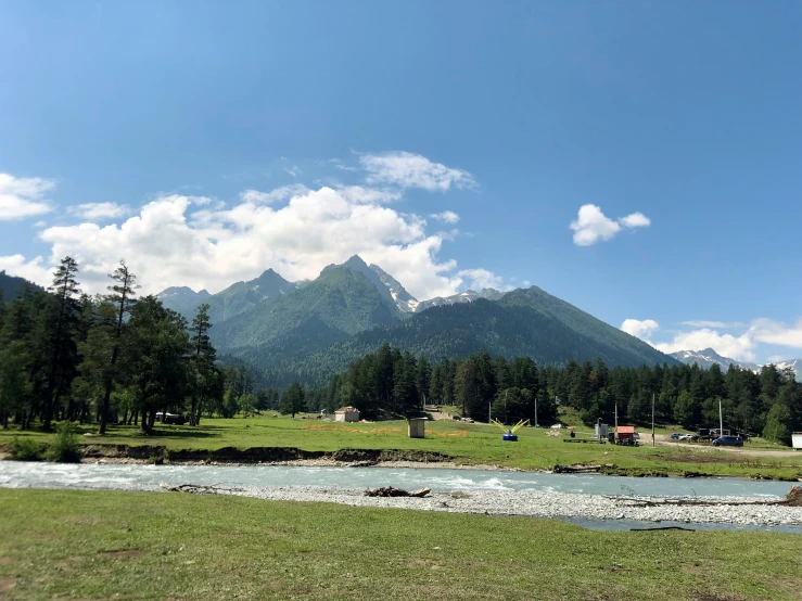 a green field with a river flowing through it near mountains