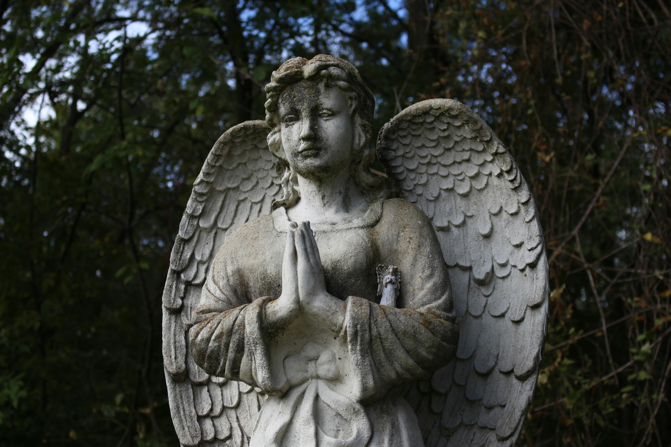 an old statue with a praying angel next to trees