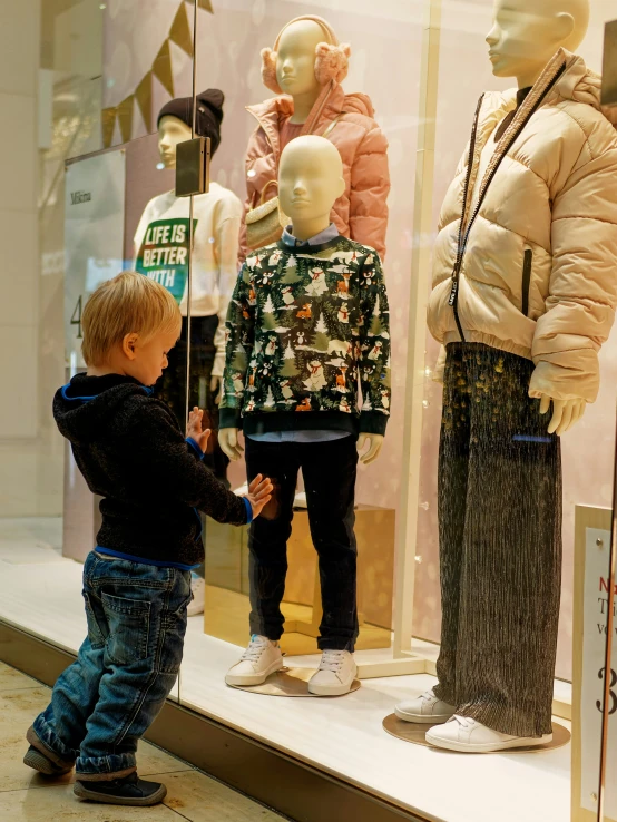 a little boy touching a mannequin in front of a window