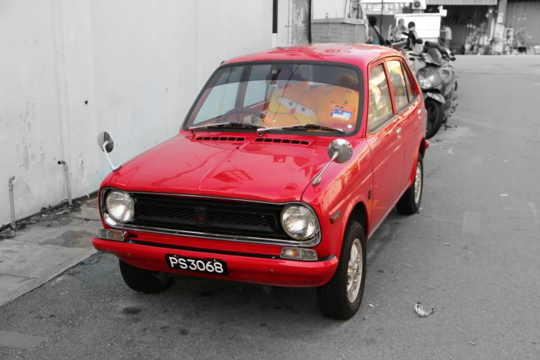 an old red hatchback car parked in front of a building