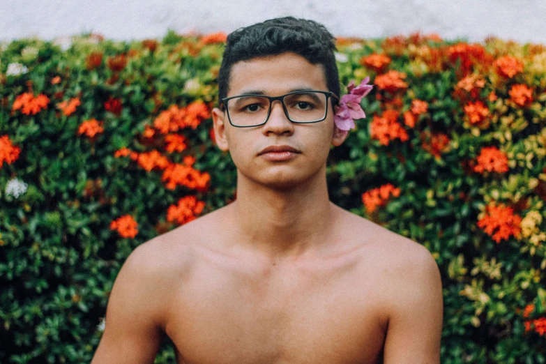 a shirtless man with glasses standing in front of a flower