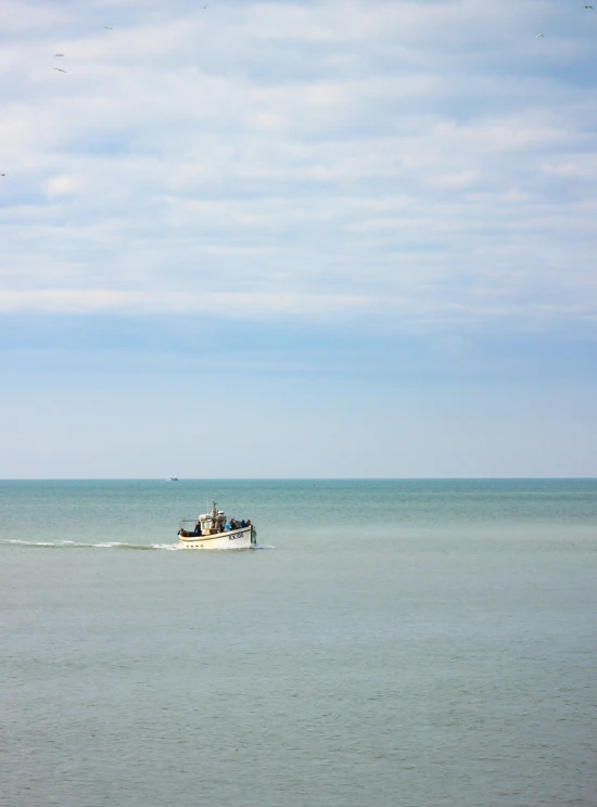 small white boat with people sitting on it traveling across a large body of water