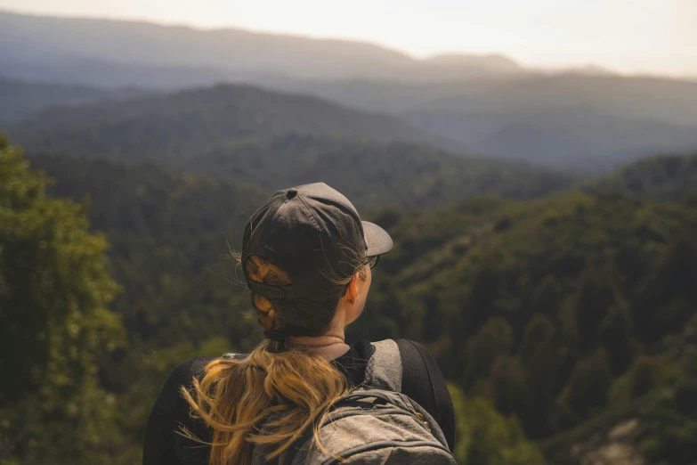 a woman with a ponytail wearing a cap looking at mountains