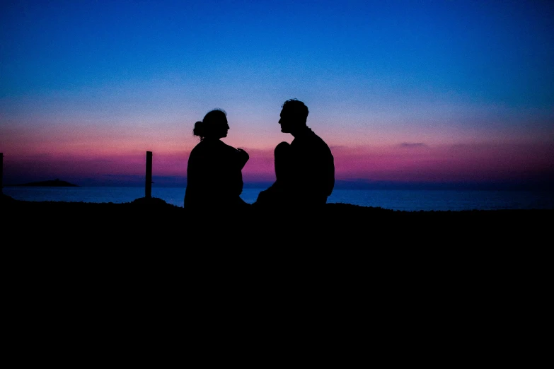 a silhouette of a couple sitting on the beach at night