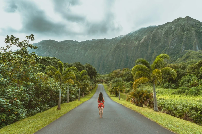 a woman walking down the middle of a road in the mountains