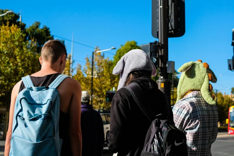 three people wait at an intersection while waiting to cross the road