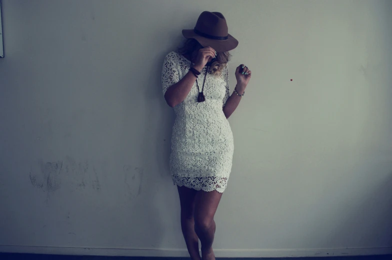 a woman with a hat poses by the wall