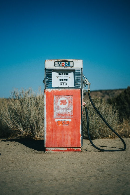 an old, red and white gas pump by some brush