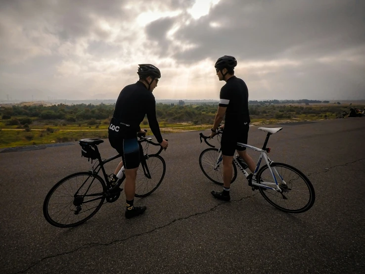 two bicyclists are walking in a lot with grey clouds in the background