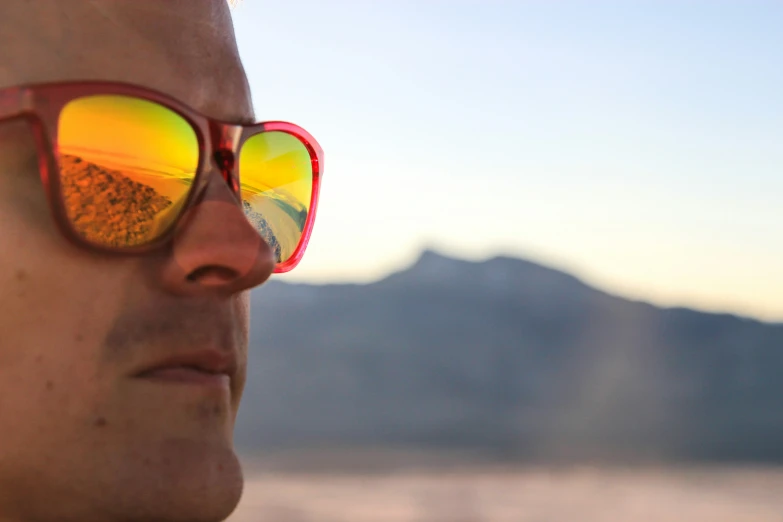 a man wearing sunglasses with mountain and sky in the background