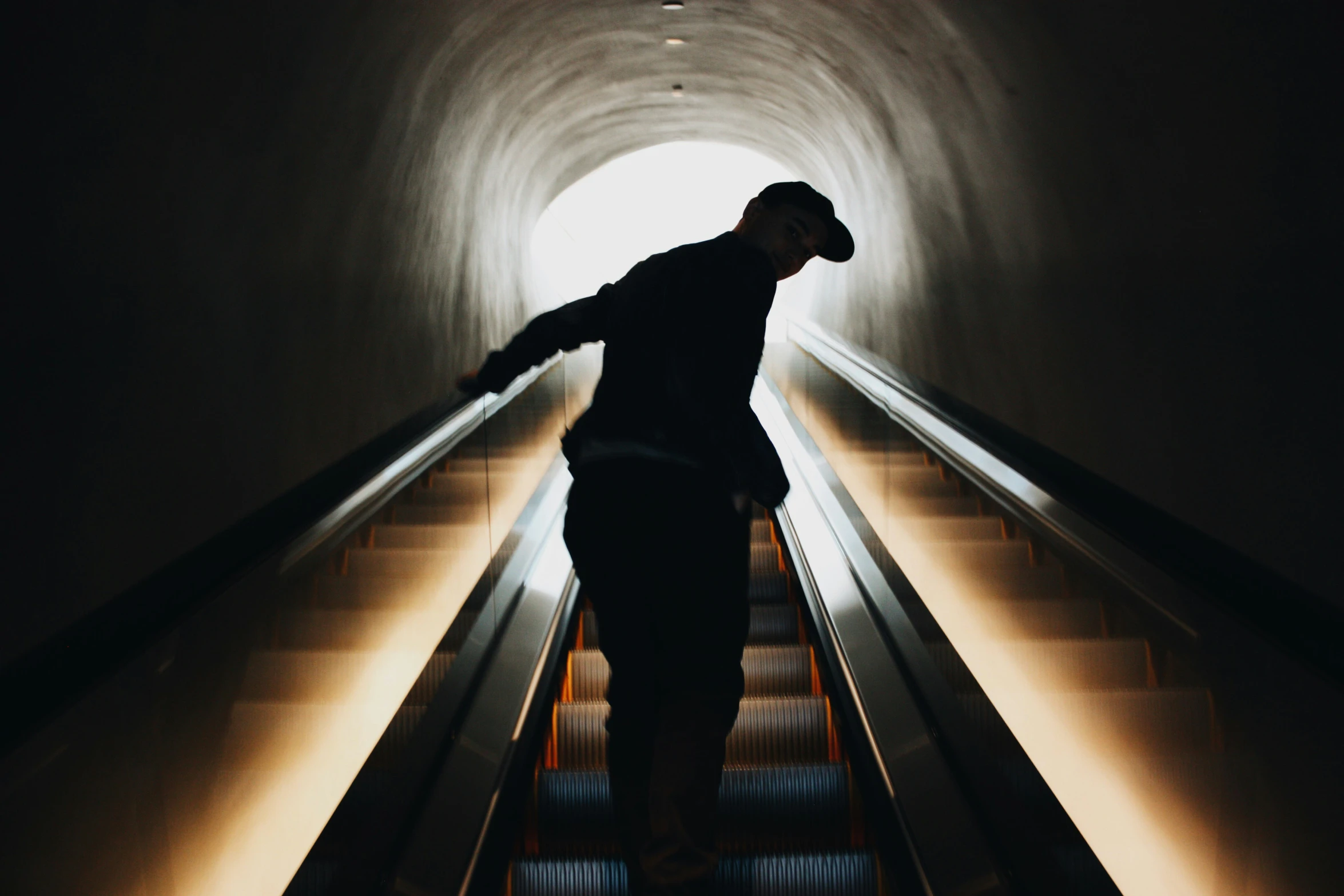 man with his arms outstretched standing on the bottom of an escalator