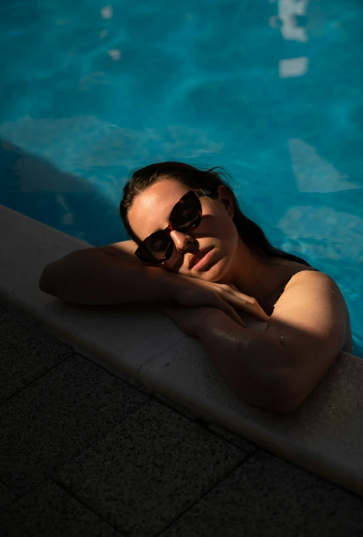 the girl in sunglasses is relaxing by the pool