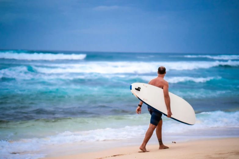 a man walking along the beach carrying a white surfboard