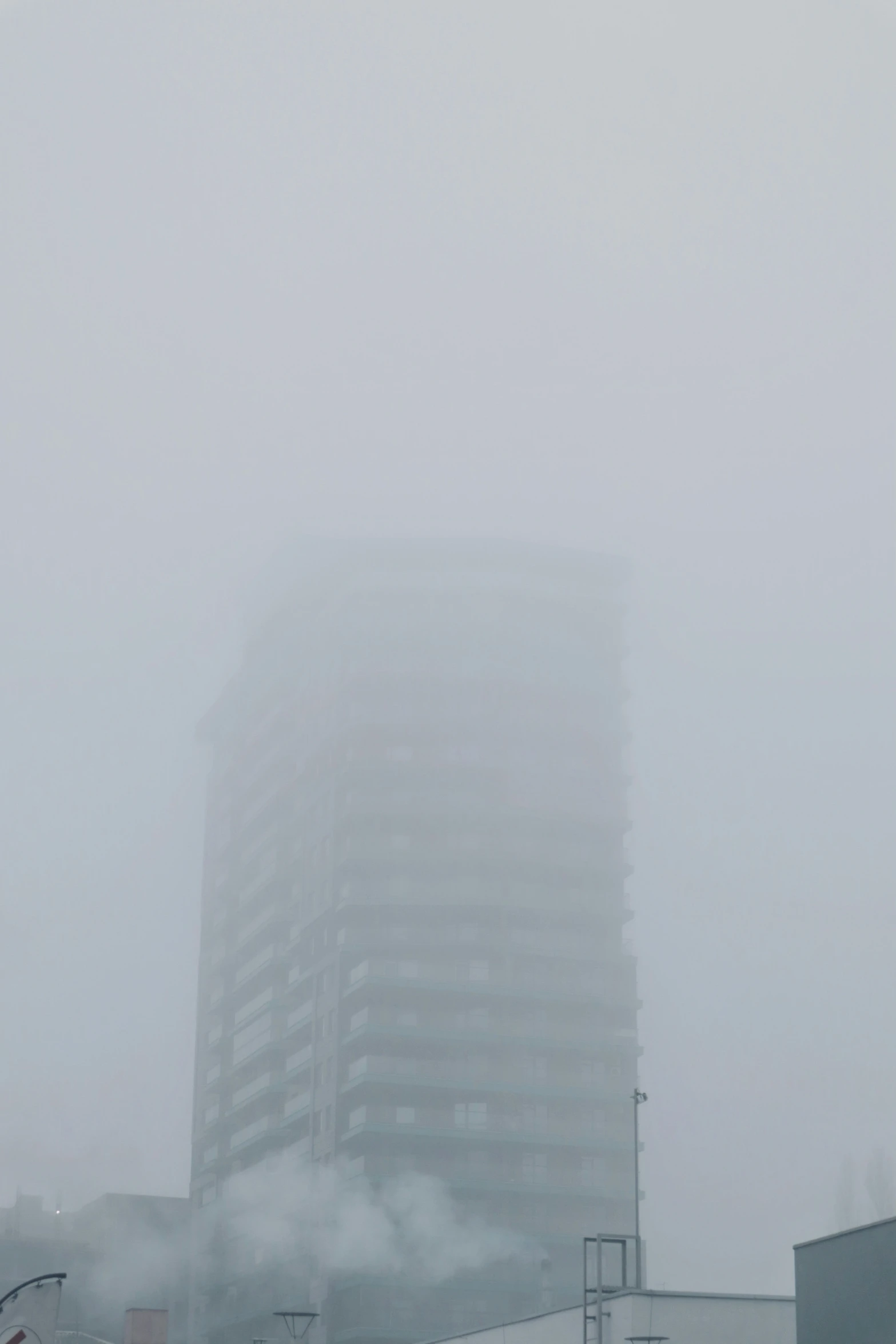 smoke billows from the bottom of the building, while buildings behind it are covered in fog