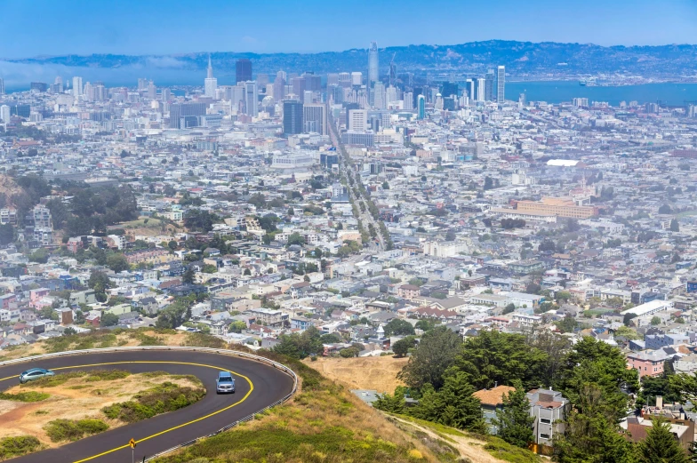 two cars drive on the road on a mountain overlooking a large city