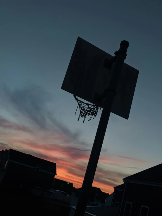 basketball hoop and the sun at dusk with houses in background
