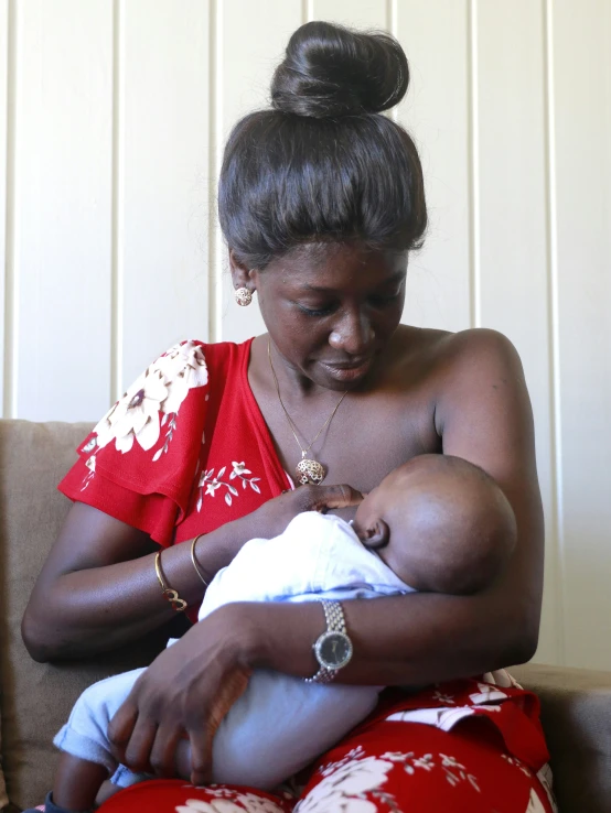 a woman in red is feeding and holding her baby