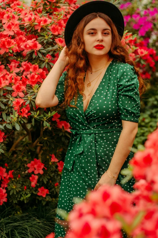 a young lady in a green dress and hat looking at a flower bed