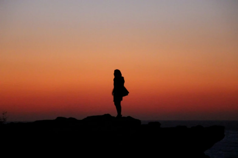 a woman standing on top of a large rock next to the ocean