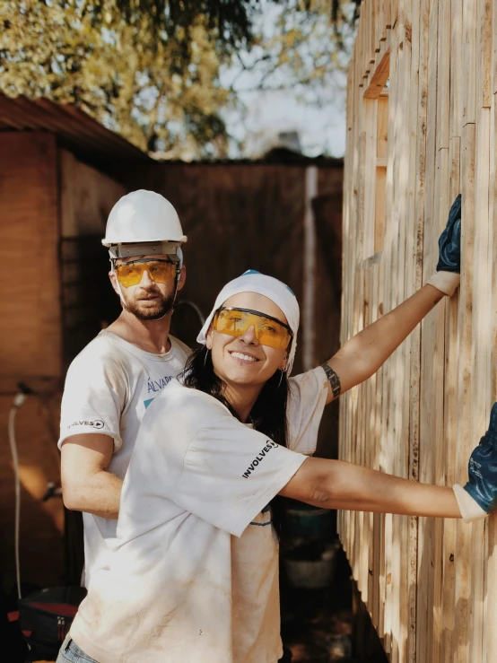 man and woman with white hardhats are putting together wood