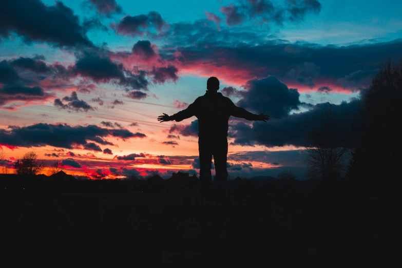 a man in silhouette standing on a hill while the sun is setting