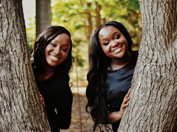 two young women standing in the woods holding onto trees