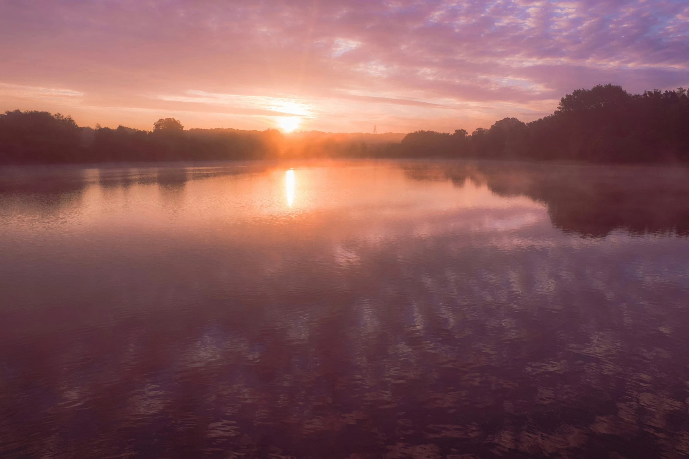 a sun set over the water with some trees on the side