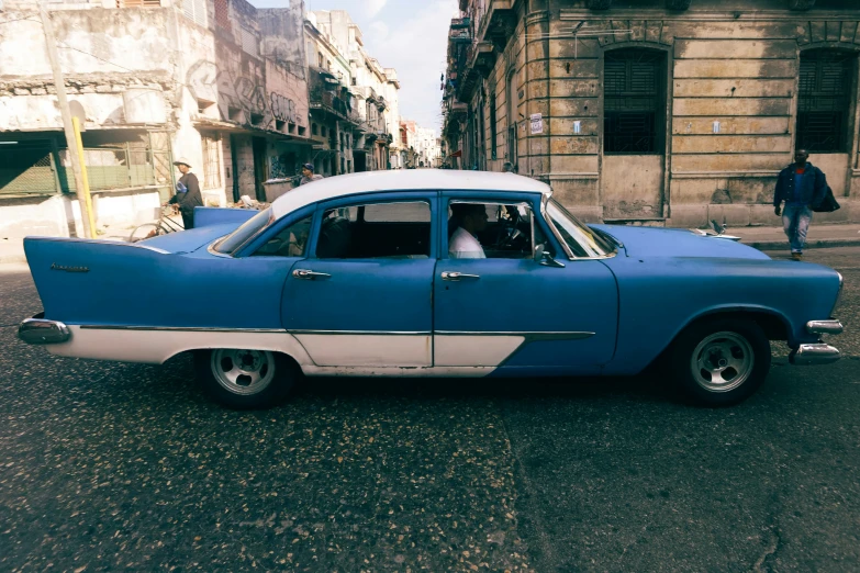 a blue classic car on the road in a large city