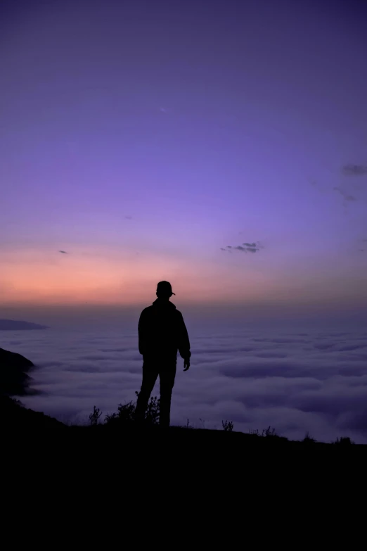 man on top of a hill overlooking a vast city with low hanging clouds