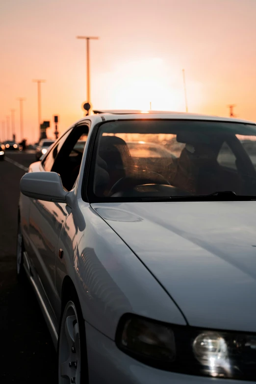 a car sits parked in a parking lot, with the sun setting behind it