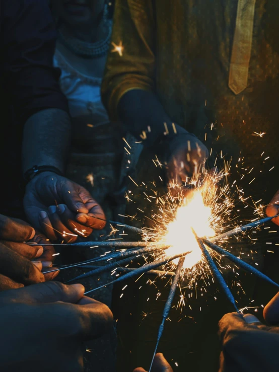 several hands holding sparklers being lit by someone