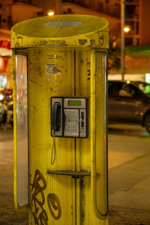 a yellow pay phone booth sits on the side of the street