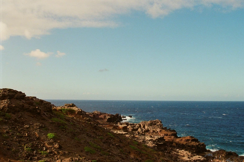 two people sitting on top of the cliff looking at the ocean