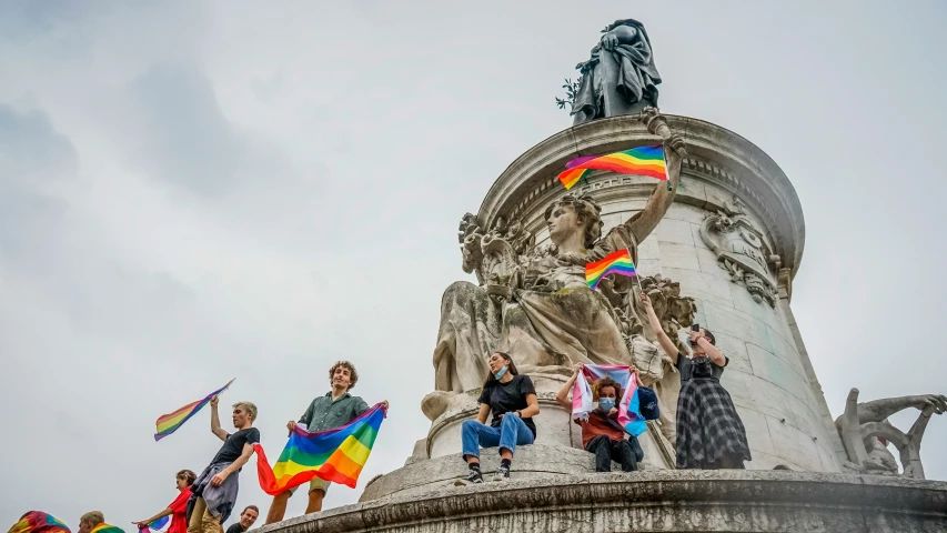 people holding up rainbow flags in front of a statue