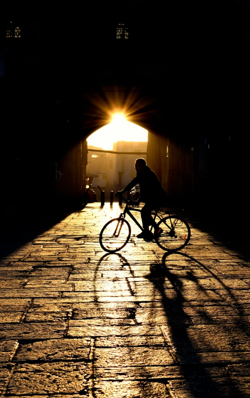 the silhouette of a person riding a bike down a street with the sun shining through a tunnel