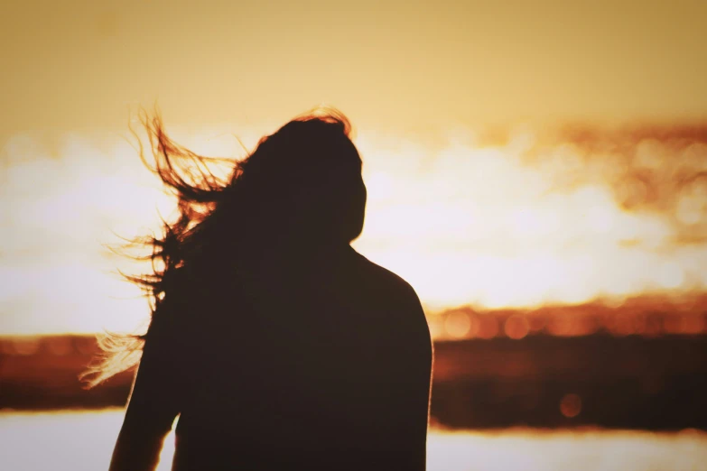 a person with her hair in the wind as the sun sets